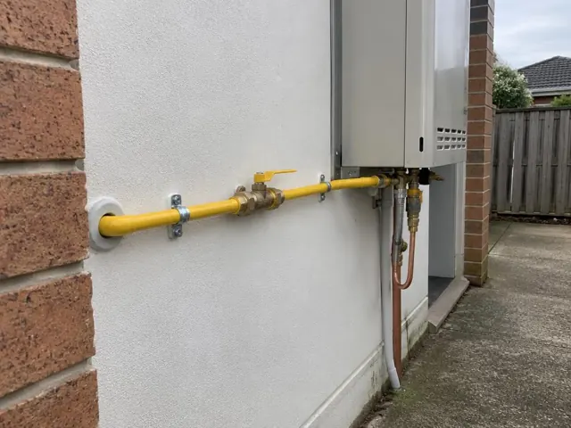 Yellow gas pipe and valve on an exterior wall beside a home appliance in Schofields